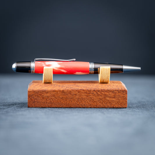 Handmade red and white resin ballpoint pen on a wooden stand against a dark background.