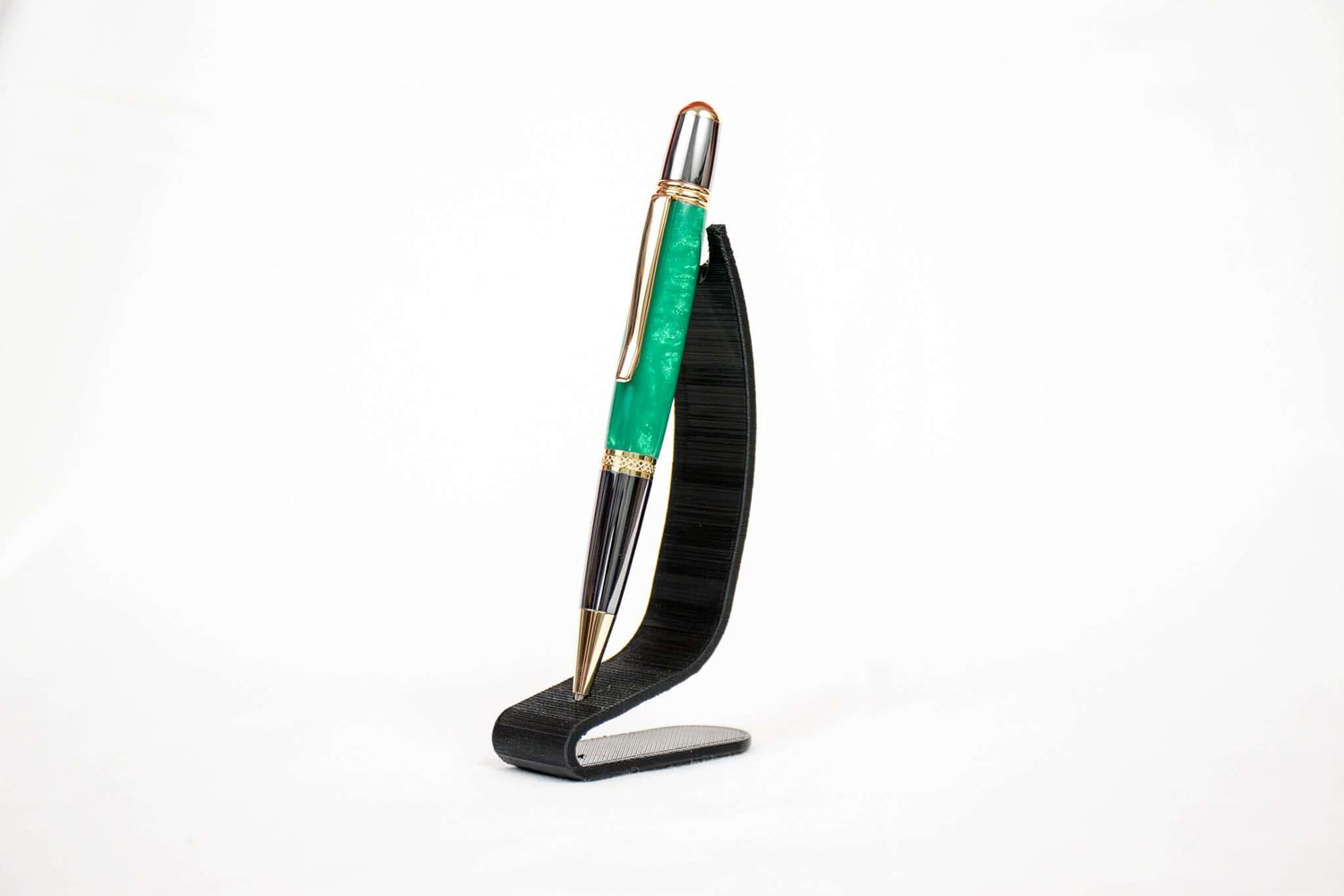 A handmade green resin twist pen with gold and gun metal plating on a black stand