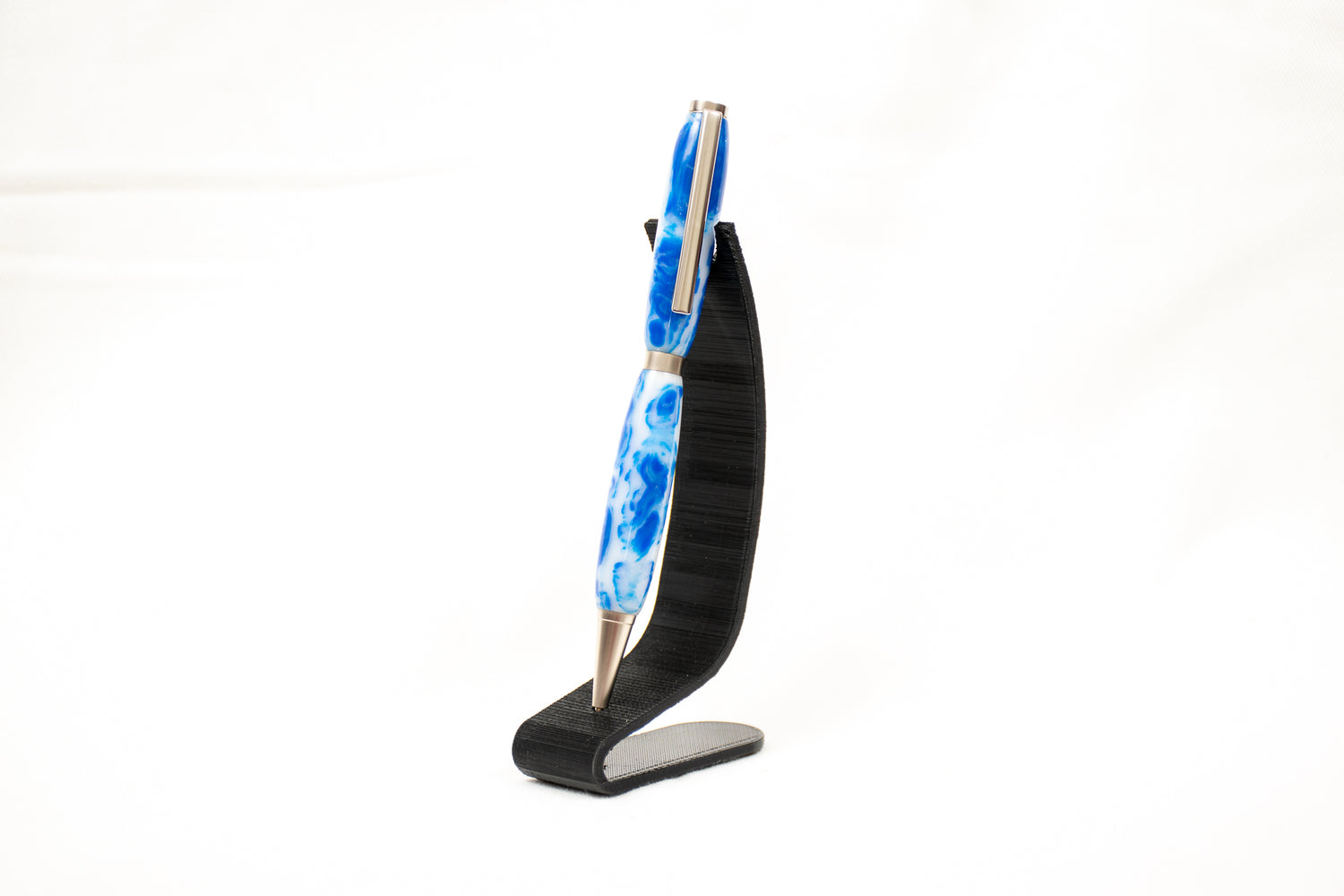 a handmade blue and white swirl resin pen with satin chrome plating on a black stand