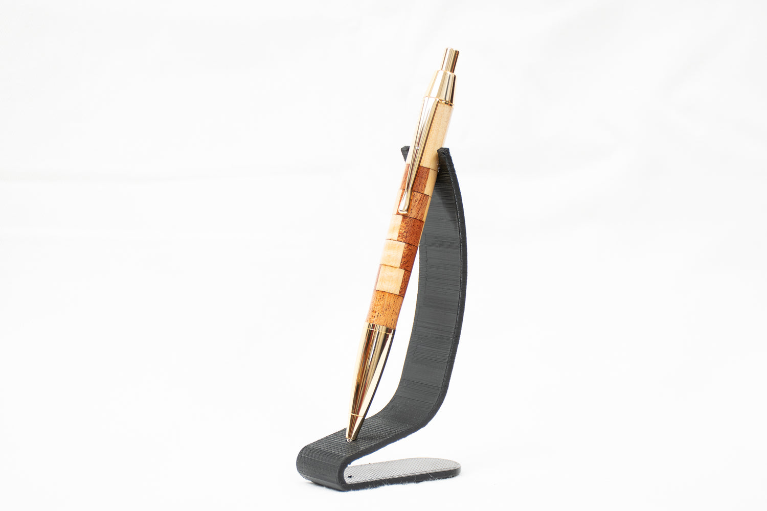 A handmade maple and african mahogany wood pen with gold plating on a black stand
