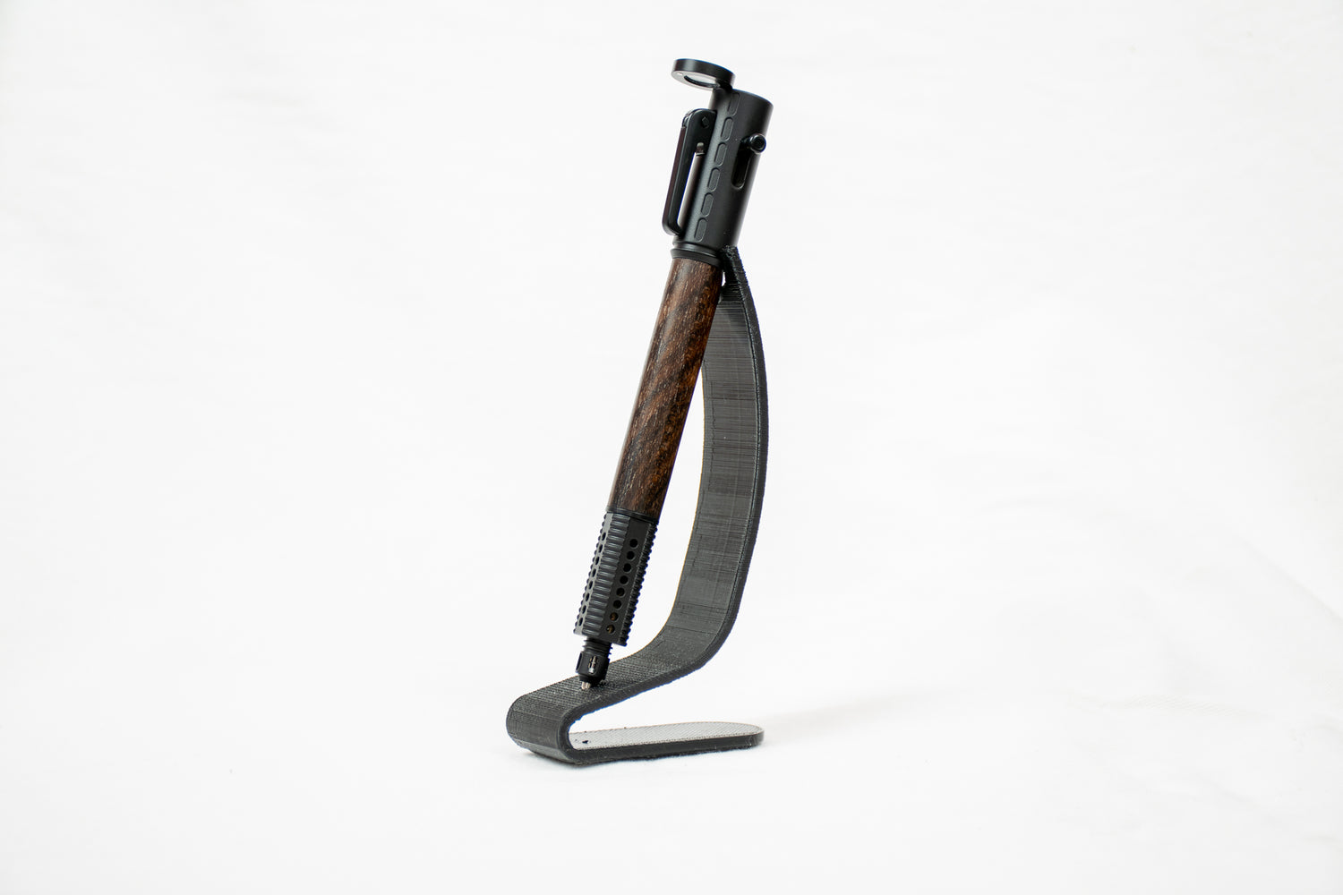 A handmade Ziricote wood bolt action pen in a gun themed kit on a black stand