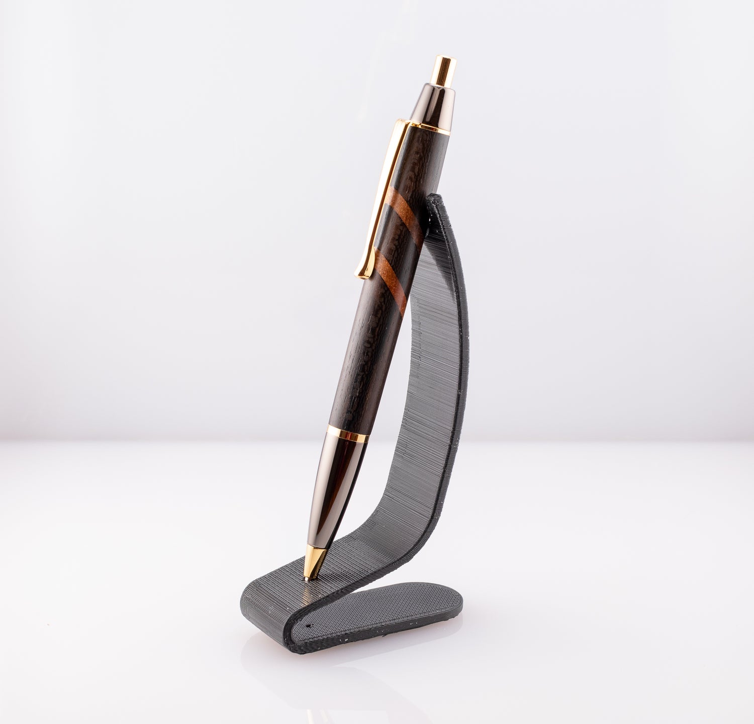 A handmade ziricote and african mahogany wood pen with gold and gun metal plating on a black stand