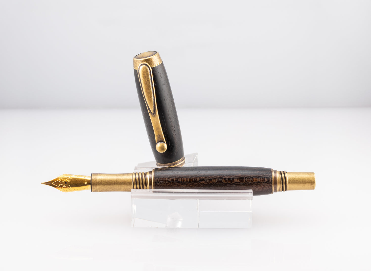 a handmade ziricote wood fountain pen with antique brass plating on a clear stand