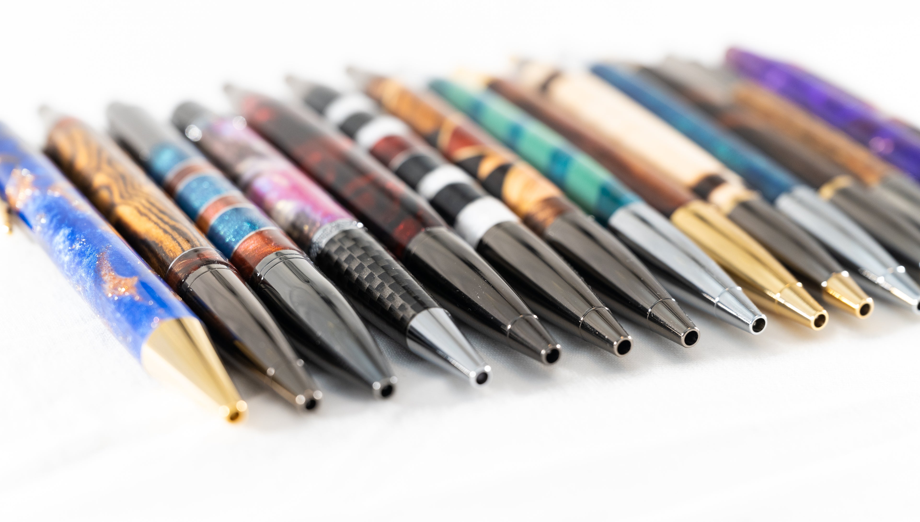 A row of handmade wood and resin click and twist ballpoint pens arranged in a line.