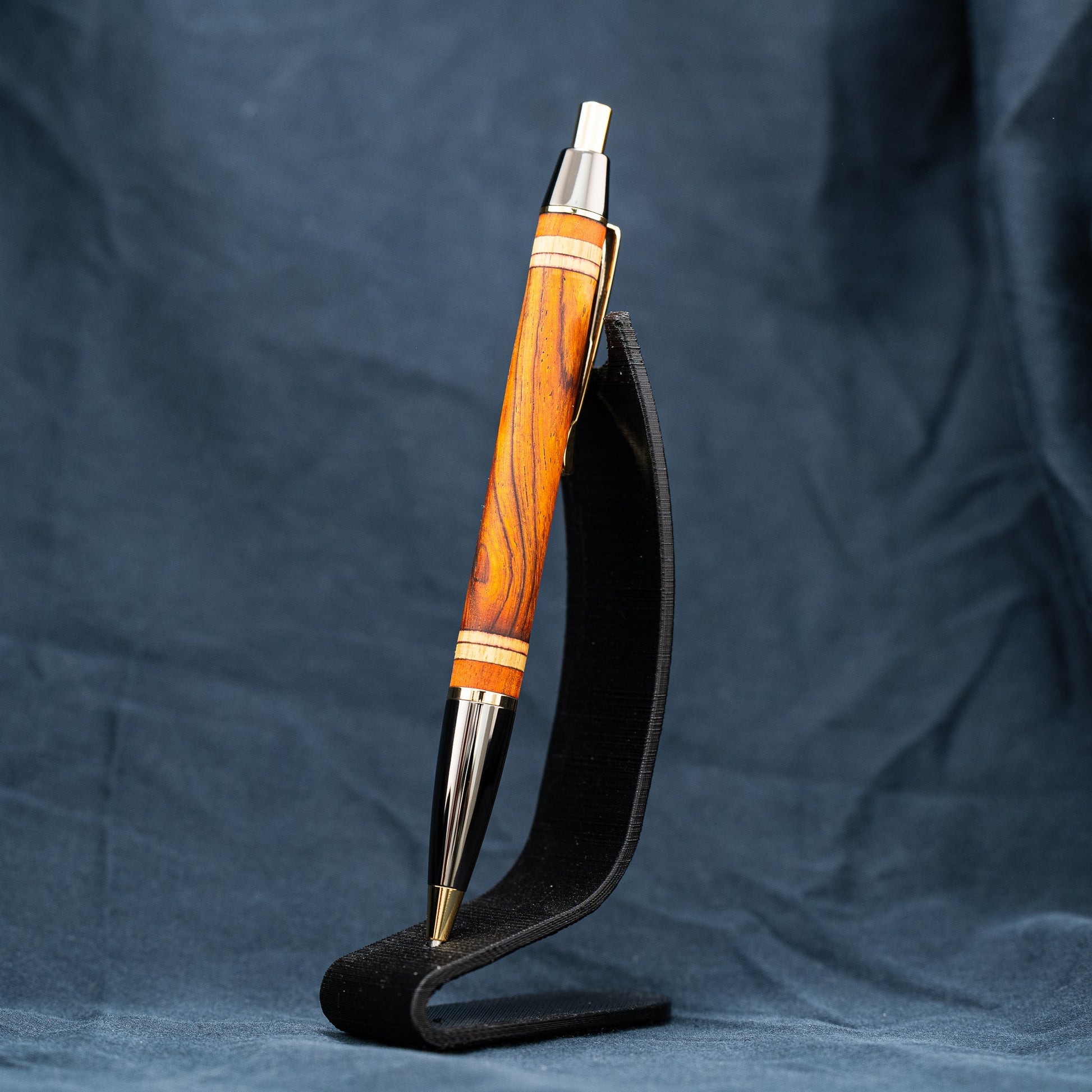 A handmade wooden pen of Cocobolo, Canarywood, and Osage Orange wood. This click pen features gold and gunmetal plating and accepts a Parker-style pen refill.