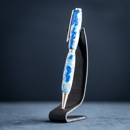 Handmade blue and white resin ballpoint pen with satin chrome plating on a dark stand against a dark background.