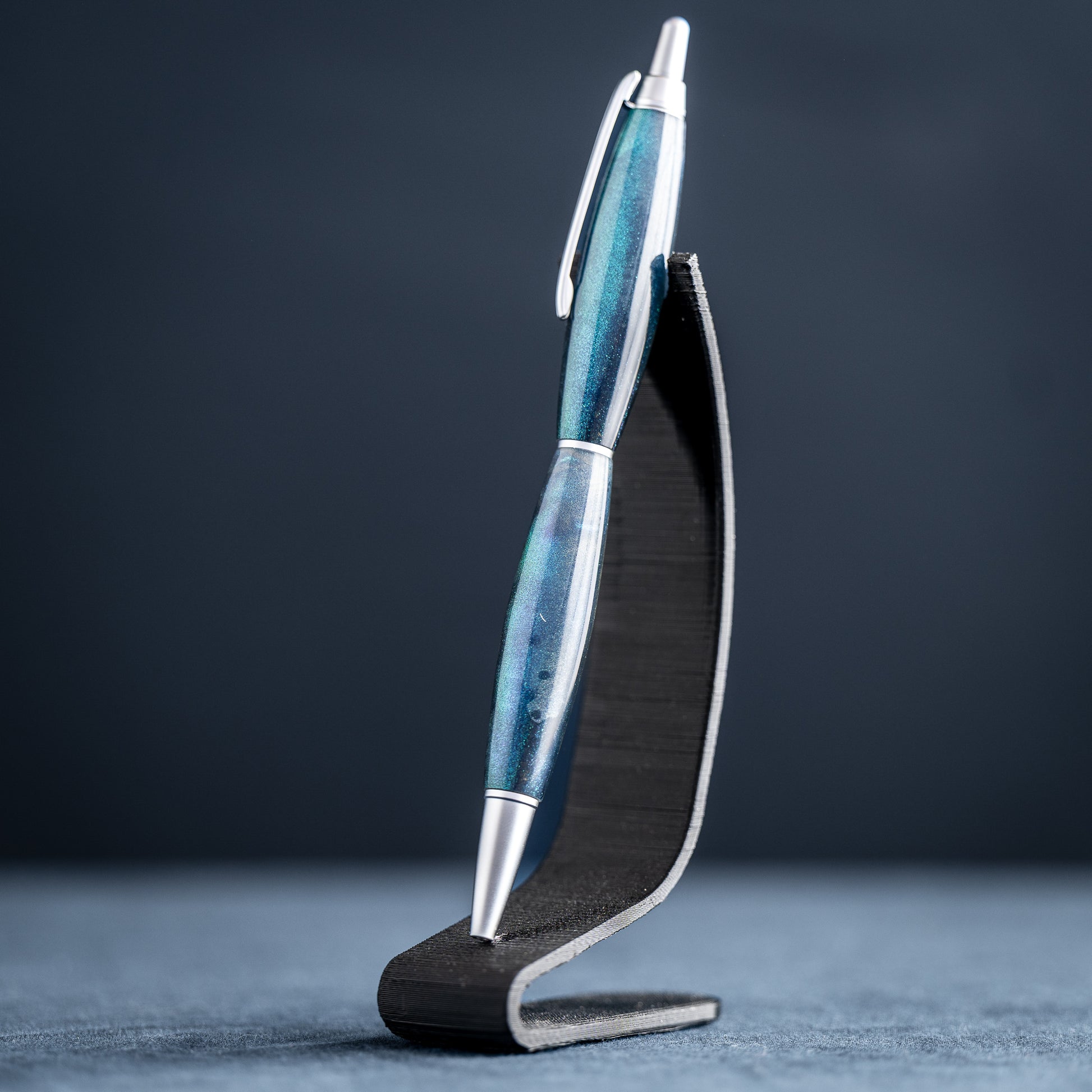 Blue pen with silver accents on a black stand against a dark background