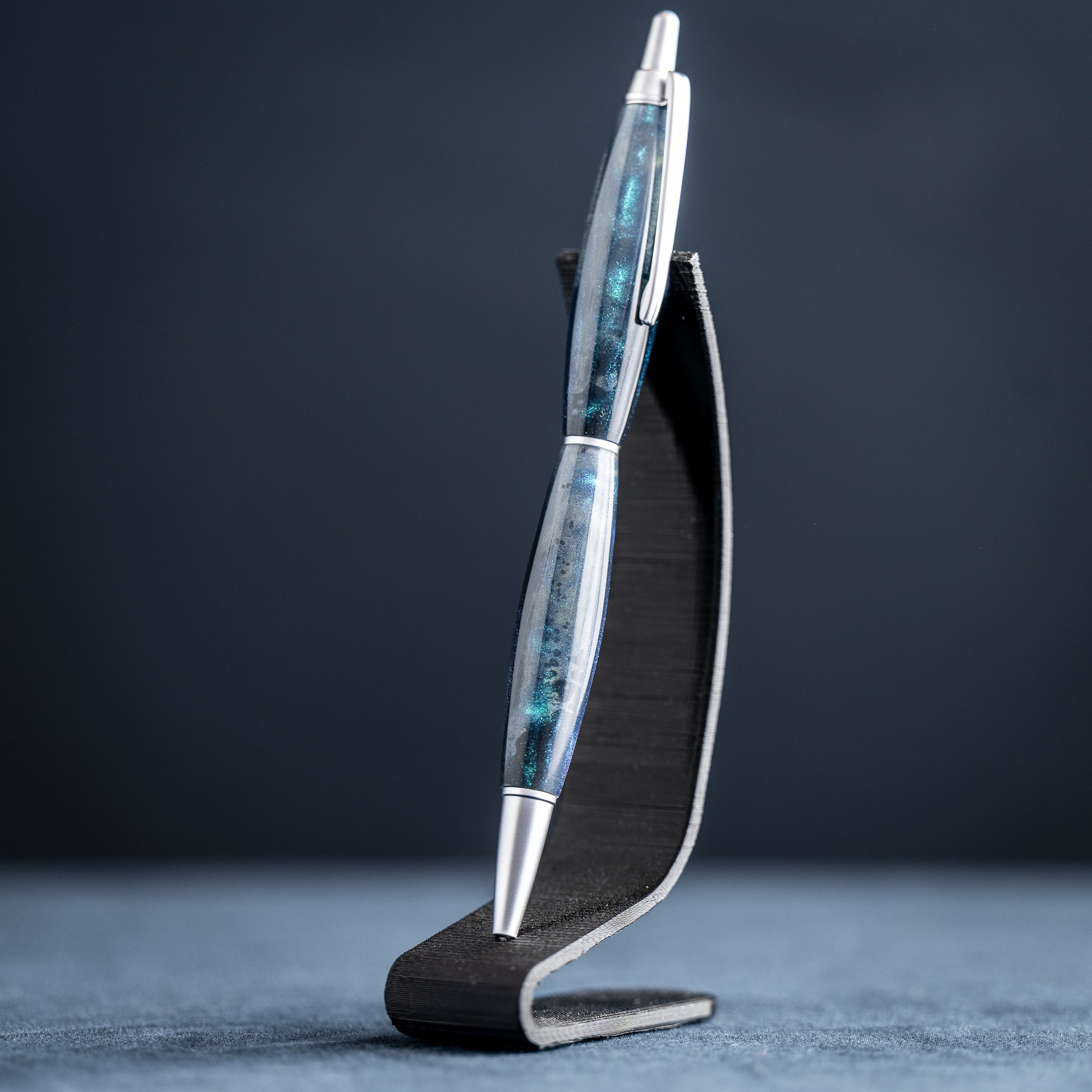 Silver pen with blue accents on a black stand against a dark background