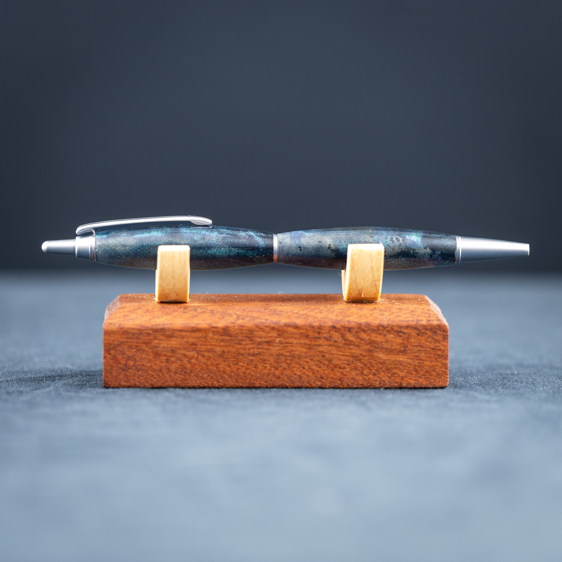 Blue resin pen on a wooden stand against a dark background.