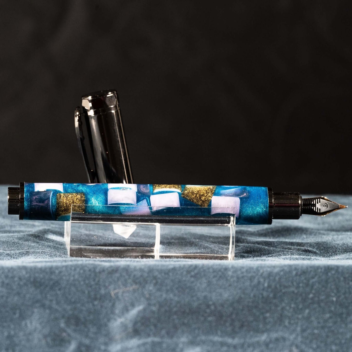 A handmade blue, white, and gold resin fountain pen with gun metal plating and a magnetic cap.