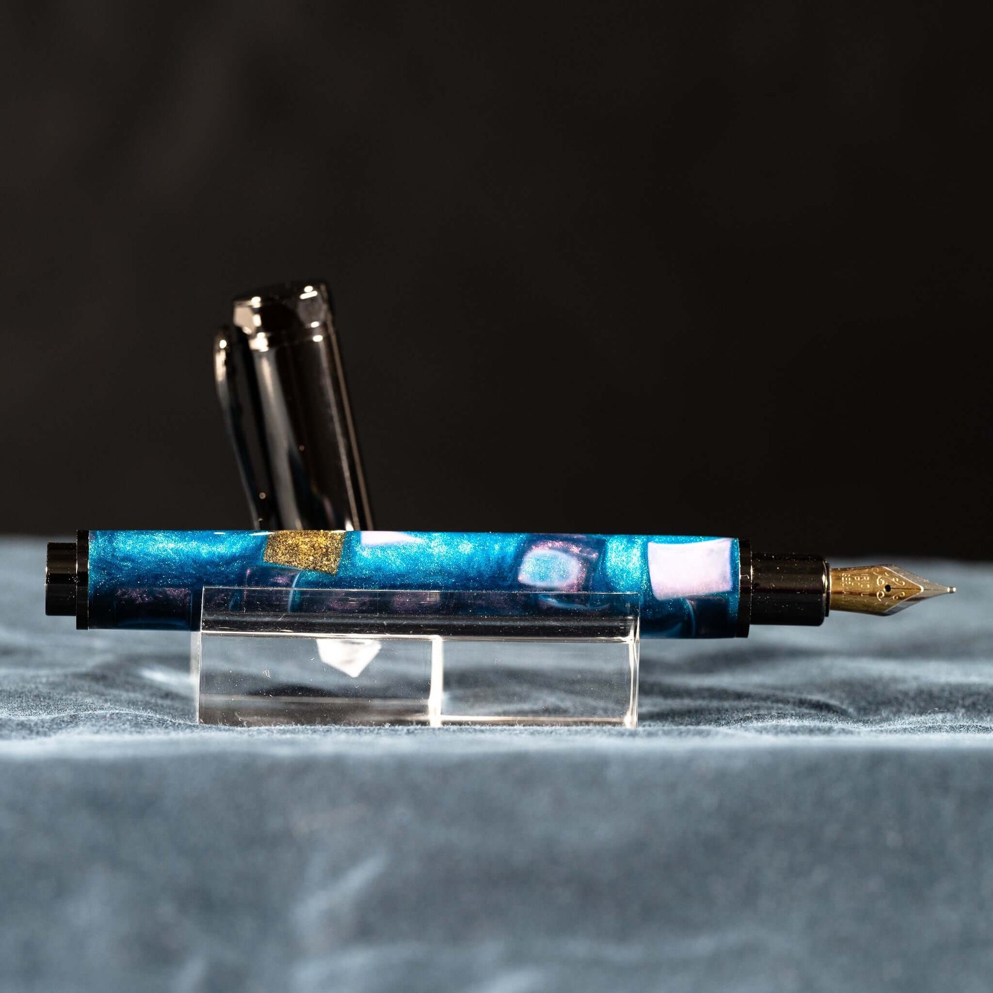 A handmade blue, white, and gold resin fountain pen with gun metal plating and a magnetic cap.