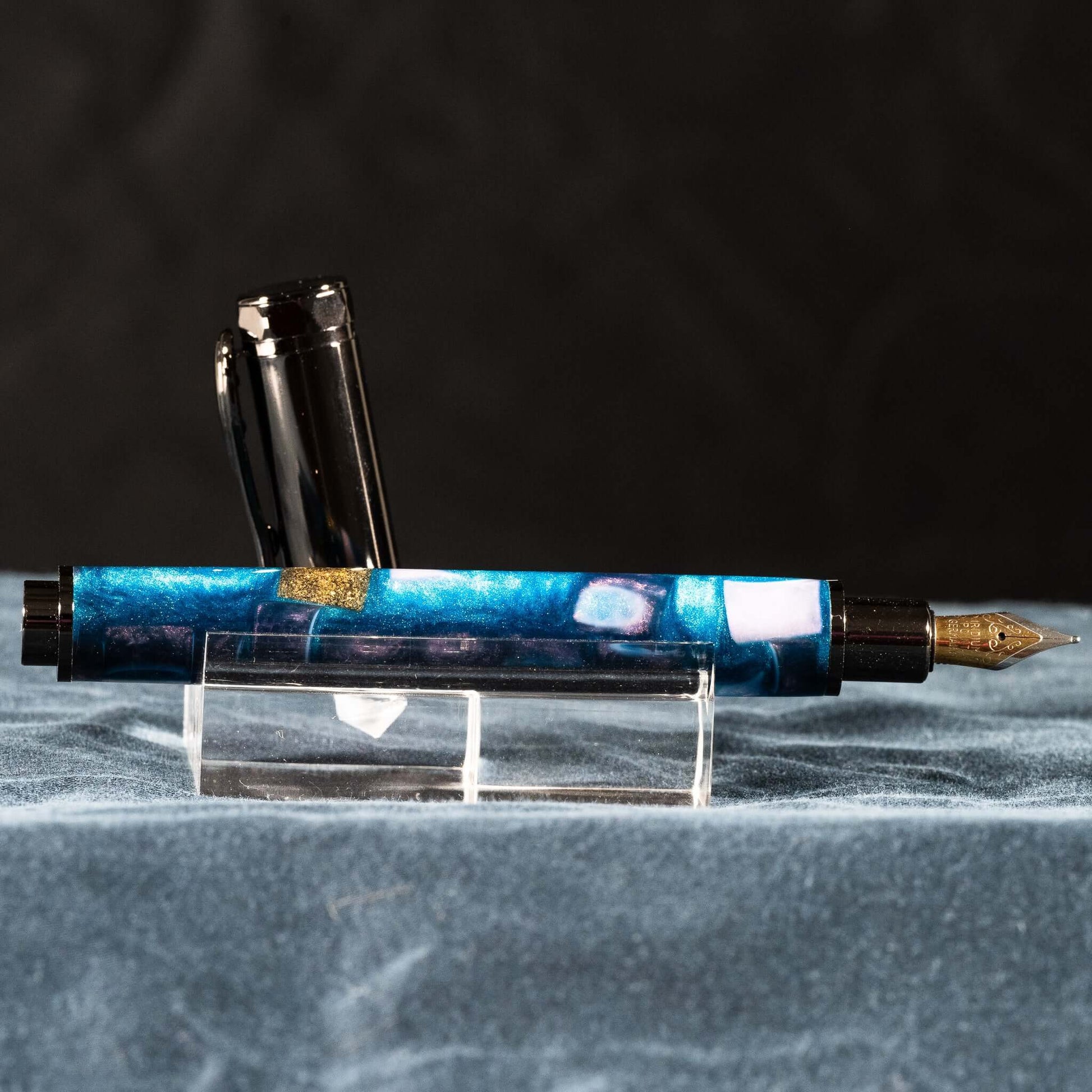 A handmade blue, white, and gold resin fountain pen with gun metal plating and a magnetic cap.