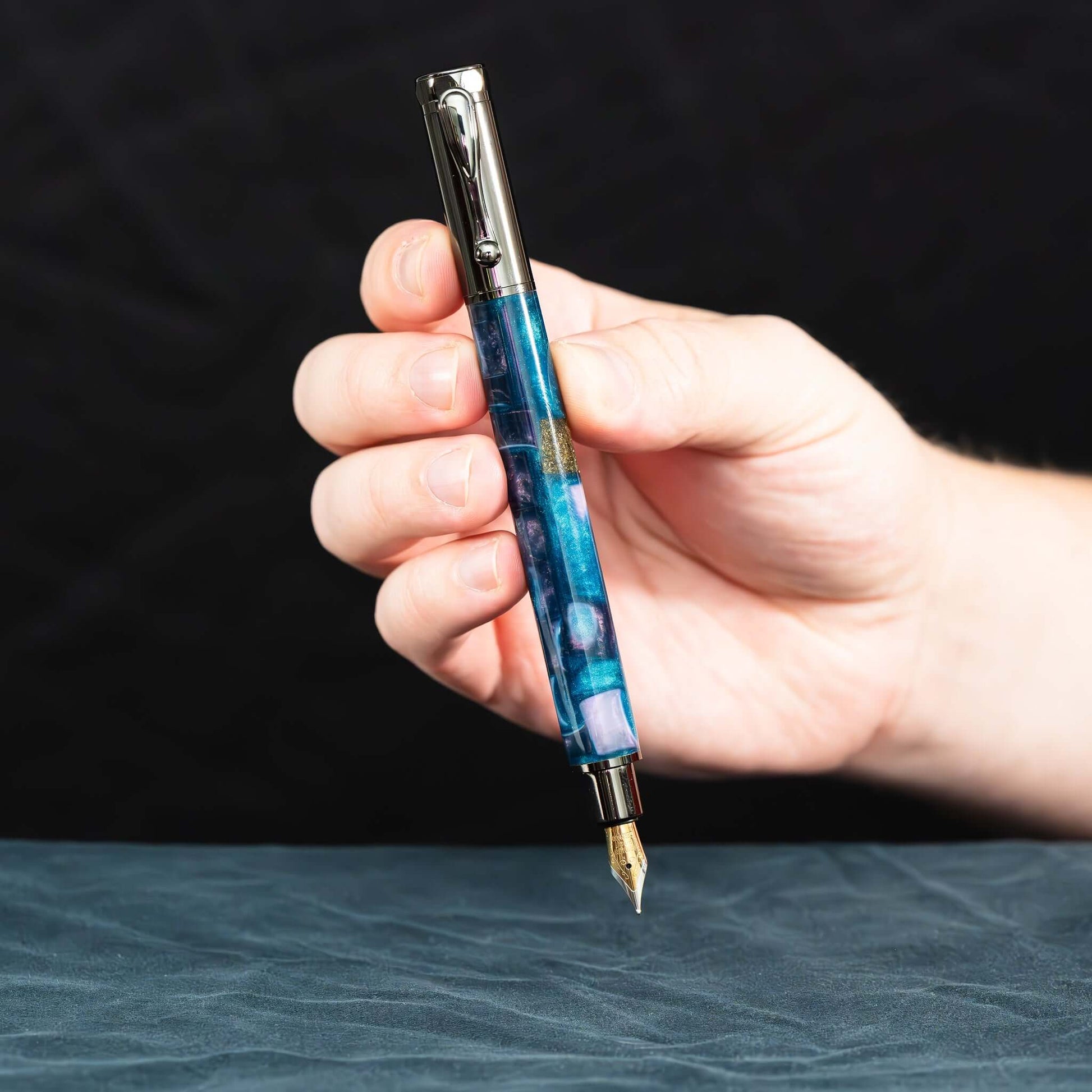 A handmade blue, white, and gold resin fountain pen with gun metal plating and a magnetic cap.