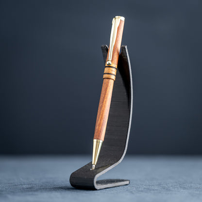 Wooden pen with gold accents on a black stand against a dark background