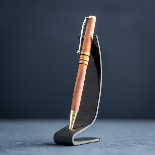 Wooden pen with gold accents on a black stand against a dark background