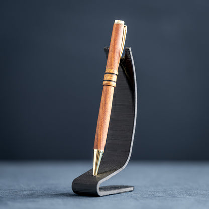 Wooden pen with gold accents on a black stand against a dark background