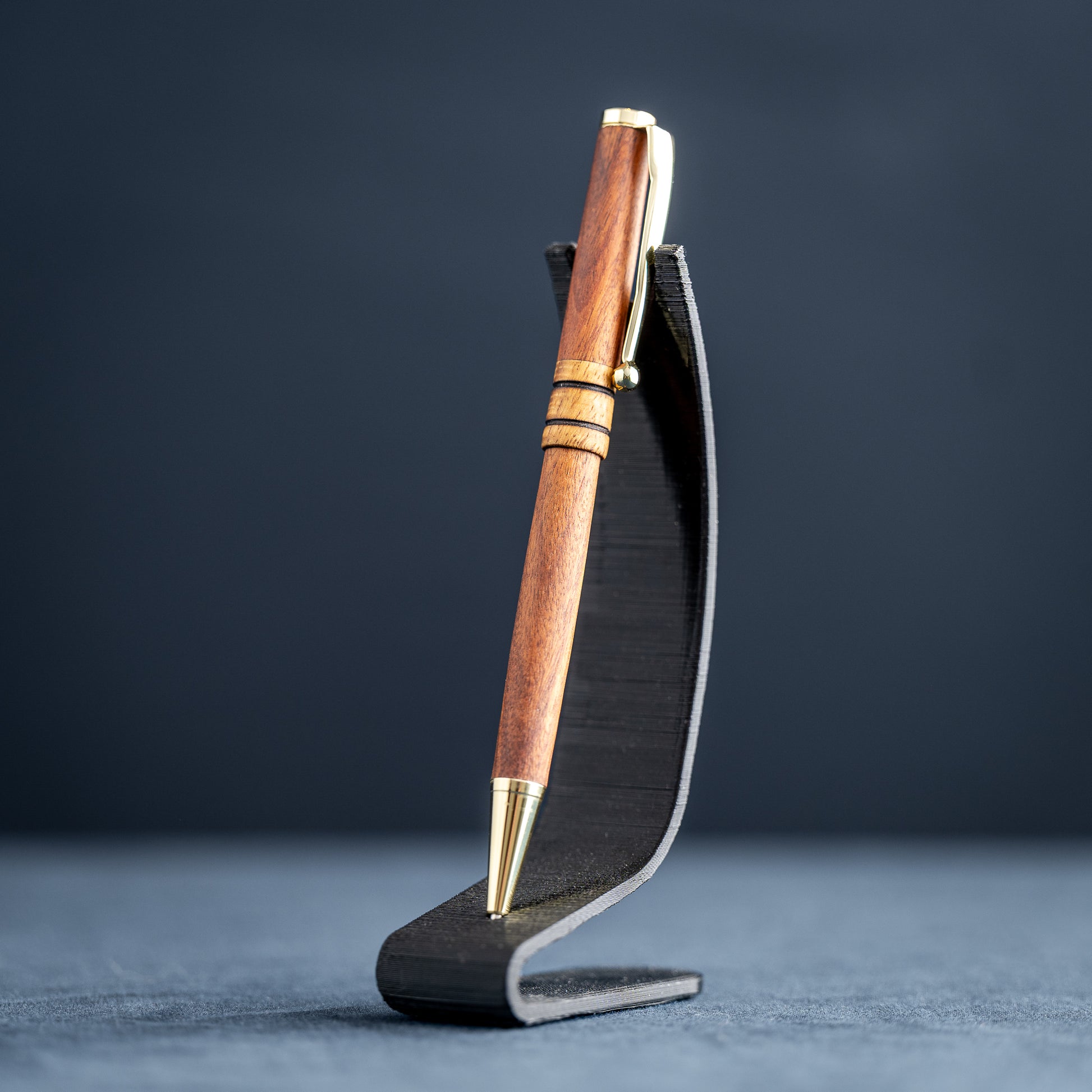 Wooden pen with gold accents on a black stand against a dark background