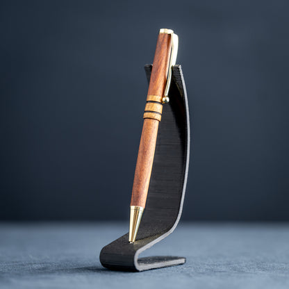 Wooden pen with gold accents on a black stand against a dark background