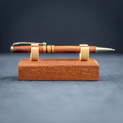 Wooden pen with gold accents on a matching wooden stand against a dark background