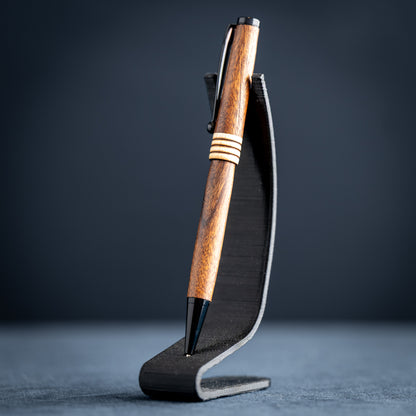 Goncalo alves and maple wood ballpoint pen with black plating on a dark stand against a dark background.