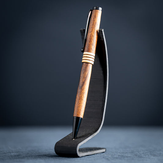 Goncalo alves and maple wood ballpoint pen with black plating on a dark stand against a dark background.
