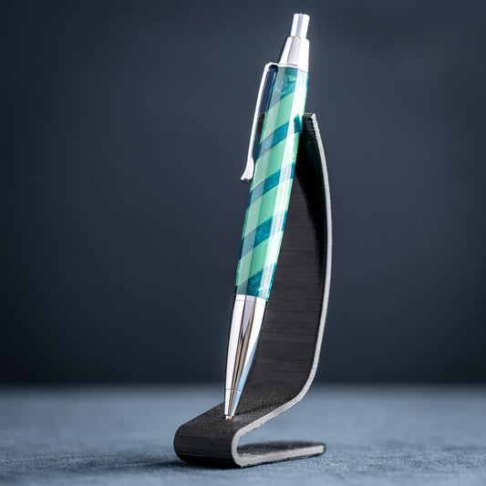 Handmade green striped resin pen with chrome plating on a dark stand against a dark background.