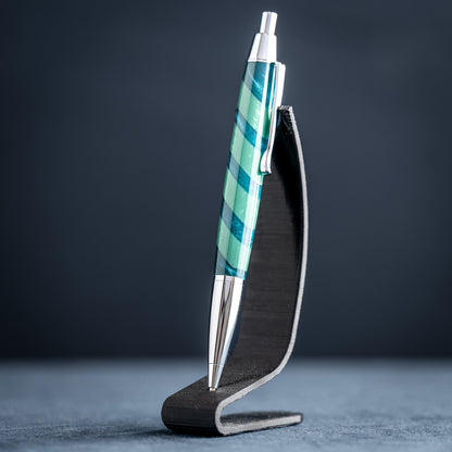 Handmade green striped resin pen with chrome plating on a dark stand against a dark background.