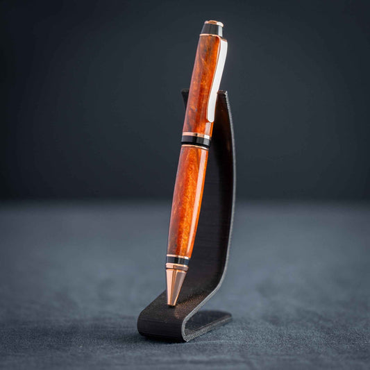 A handmade metallic orange and blue resin twist ballpoint pen with bright copper plating on a dark stand against a dark background.