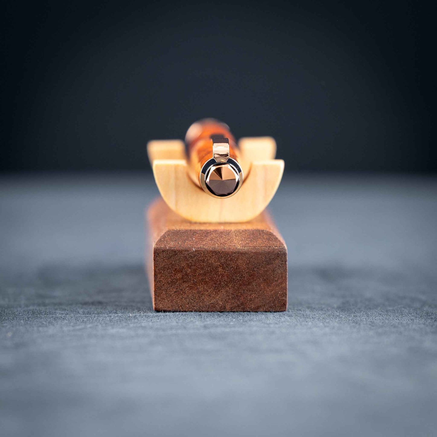 A handmade metallic orange and blue resin twist ballpoint pen with bright copper plating on a dark stand against a dark background.