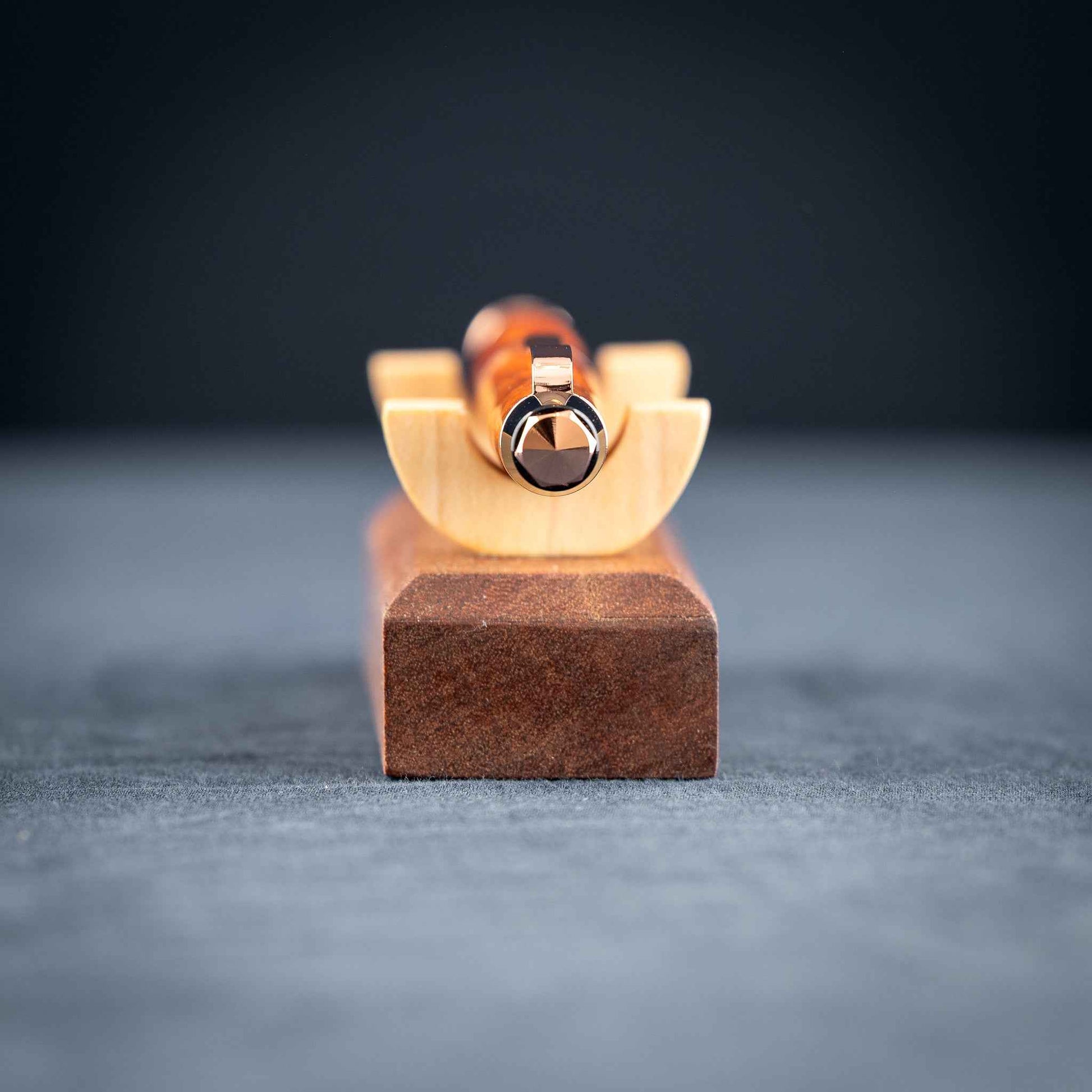 A handmade metallic orange and blue resin twist ballpoint pen with bright copper plating on a dark stand against a dark background.