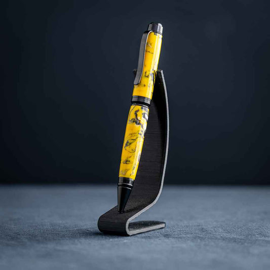 A handmade black, yellow, and white resin ballpoint pen on a black stand against a black background.