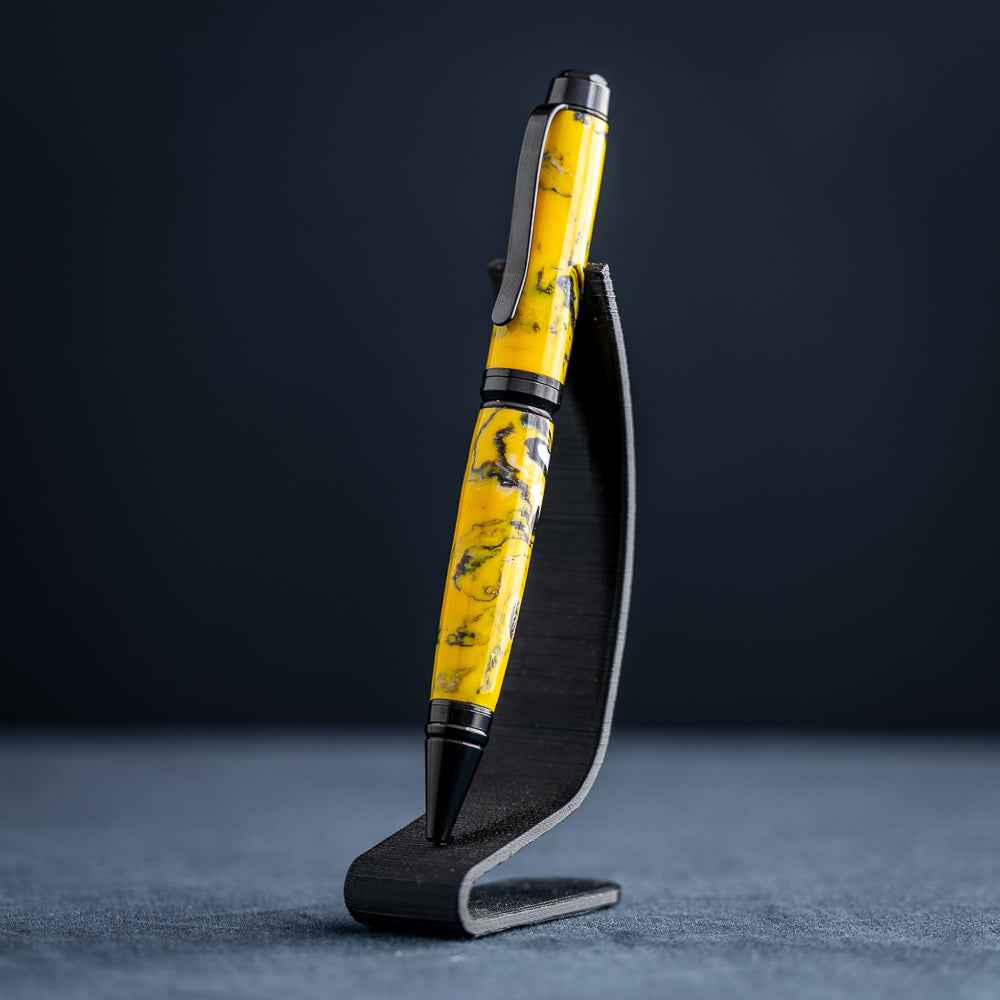 A handmade black, yellow, and white resin ballpoint pen on a wooden stand against a black background.