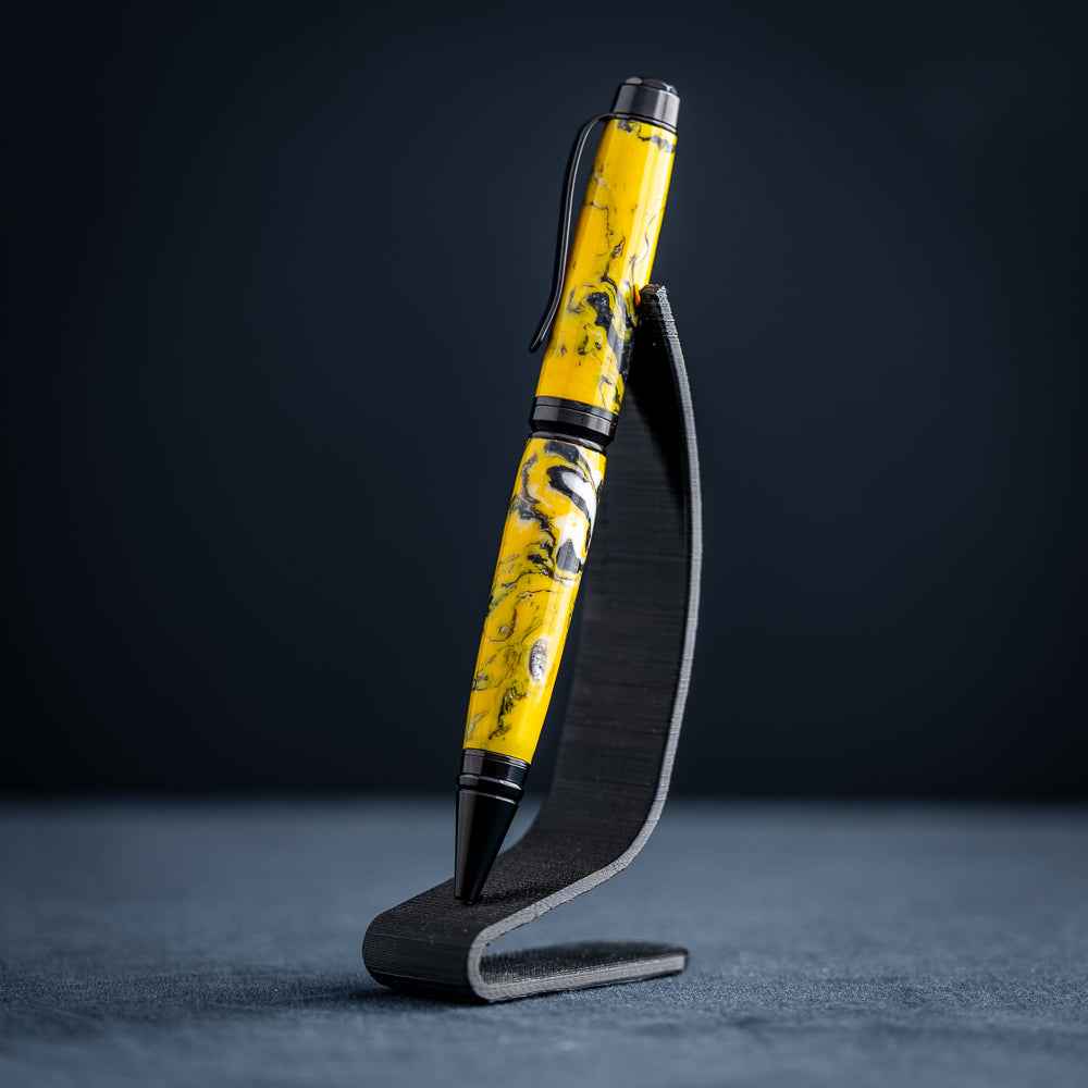 A handmade black, yellow, and white resin ballpoint pen on a wooden stand against a black background.