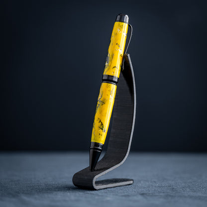 A handmade black, yellow, and white resin ballpoint pen on a wooden stand against a black background.