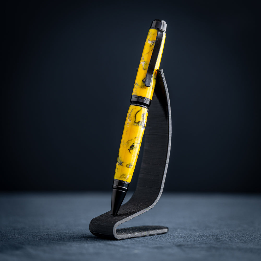 A handmade black, yellow, and white resin ballpoint pen on a wooden stand against a black background.