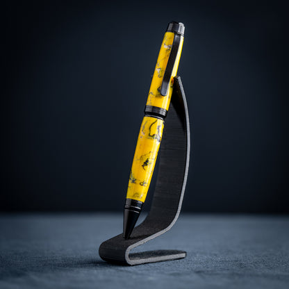 A handmade black, yellow, and white resin ballpoint pen on a wooden stand against a black background.