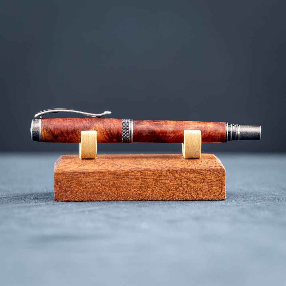 Handcrafted Australian Mallee Burl wood rollerball pen on a wooden stand against a dark background.