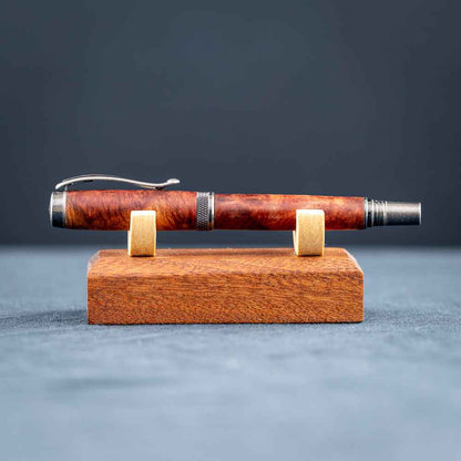 Handcrafted Australian Mallee Burl wood rollerball pen on a wooden stand against a dark background.