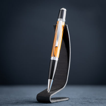 Handmade Osage orange wood and black wood ballpoint pen on a black stand against a dark background.