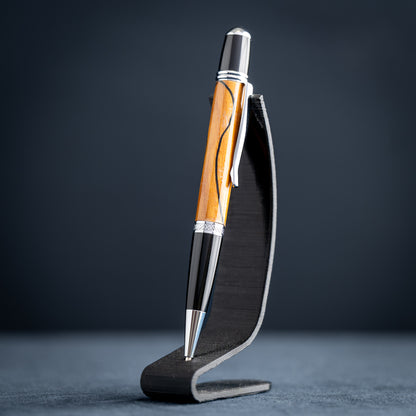 Handmade Osage orange wood and black wood ballpoint pen on a black stand against a dark background.