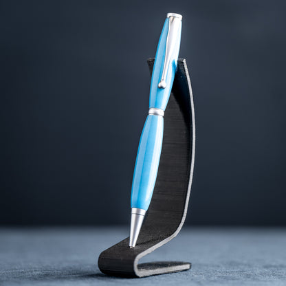 A handmade powder blue ballpoint resin twist pen with satin chrome plating on a dark stand against a dark background.