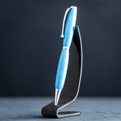 A handmade powder blue ballpoint resin twist pen with satin chrome plating on a dark stand against a dark background.