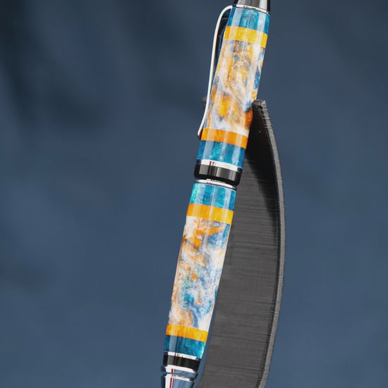 A handmade teal, orange, and white resin ballpoint Cigar pen with chrome plating.