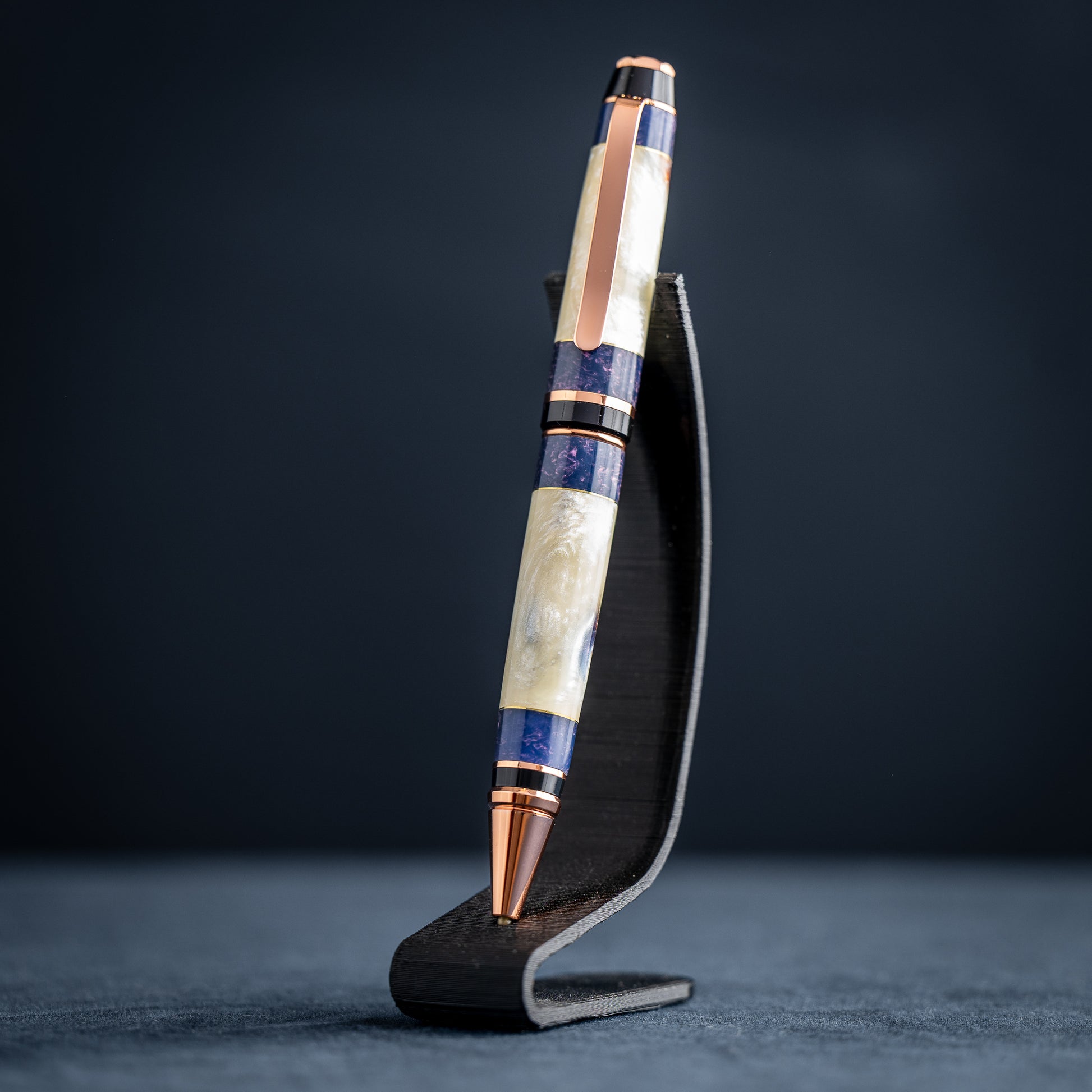Handmade opal and purple resin ballpoint twist pen with copper plating on wooden stand against a dark background.