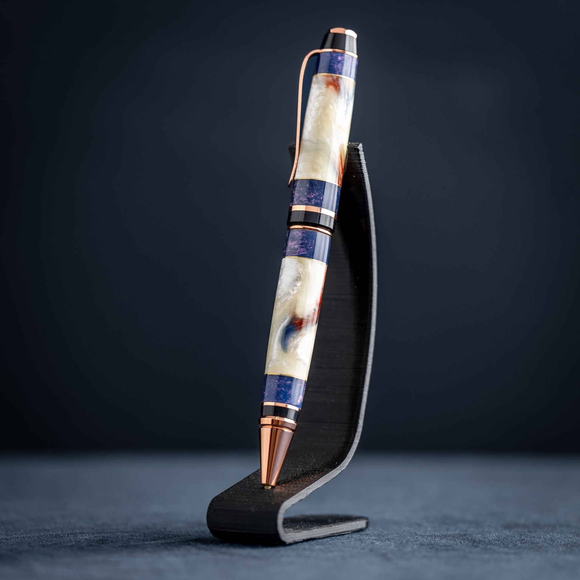 Handmade opal and purple resin ballpoint twist pen with copper plating on dark stand against a dark background.