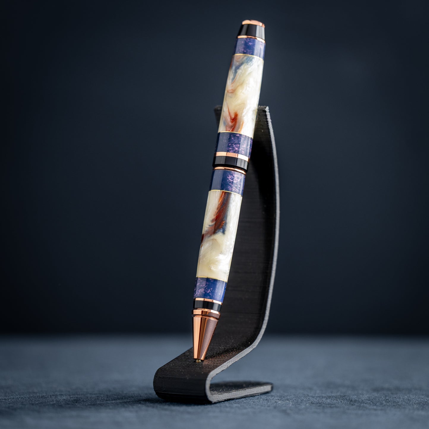 Handmade opal and purple resin ballpoint twist pen with copper plating on wooden stand against a dark background.