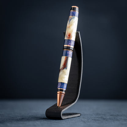 Handmade opal and purple resin ballpoint twist pen with copper plating on wooden stand against a dark background.