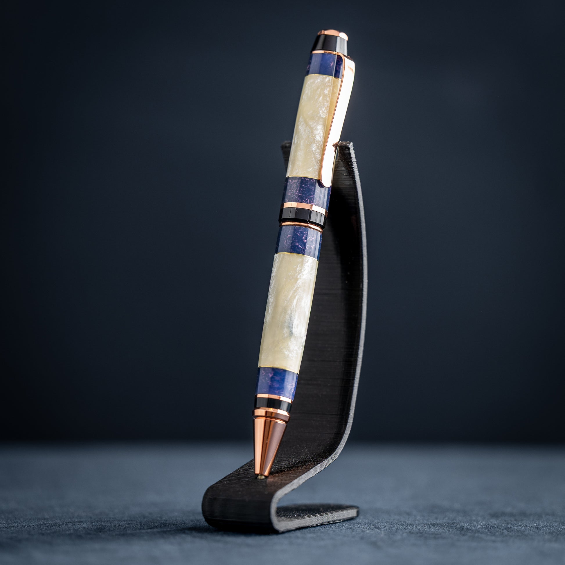 Handmade opal and purple resin ballpoint twist pen with copper plating on wooden stand against a dark background.
