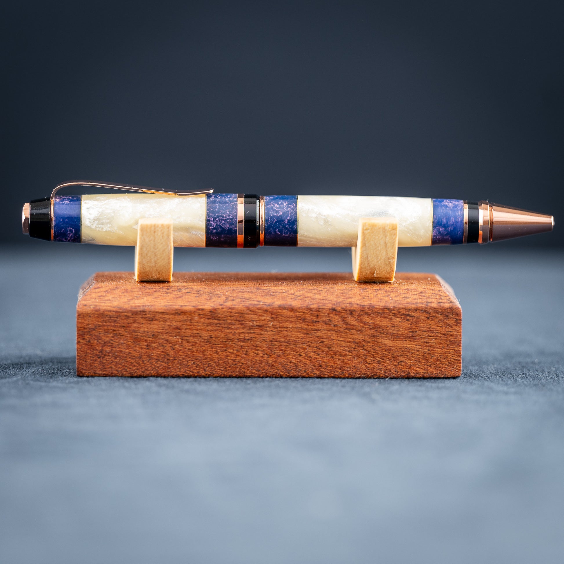 Handmade opal and purple resin ballpoint twist pen with copper plating on wooden stand against a dark background.