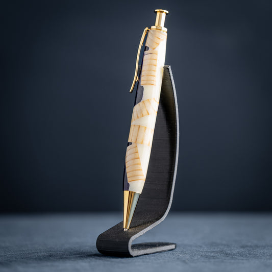 A handmade pine wood, purple, and white resin ballpoint click pen with gold plating on a dark stand against a dark background.